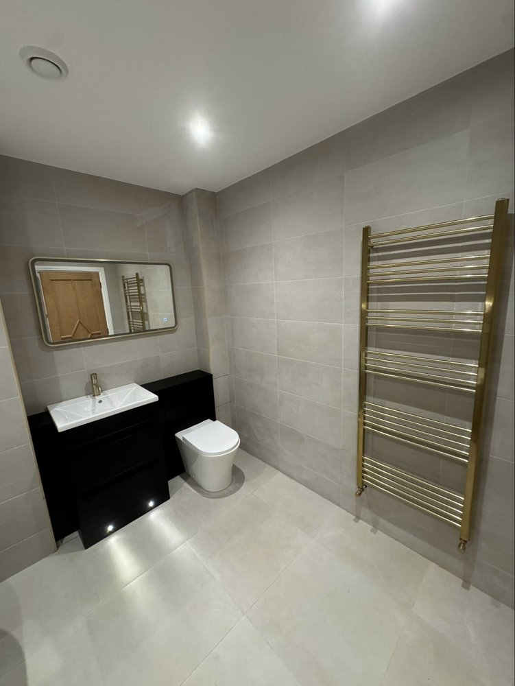 A tall brushed brass heated towel rail in a modern bathroom