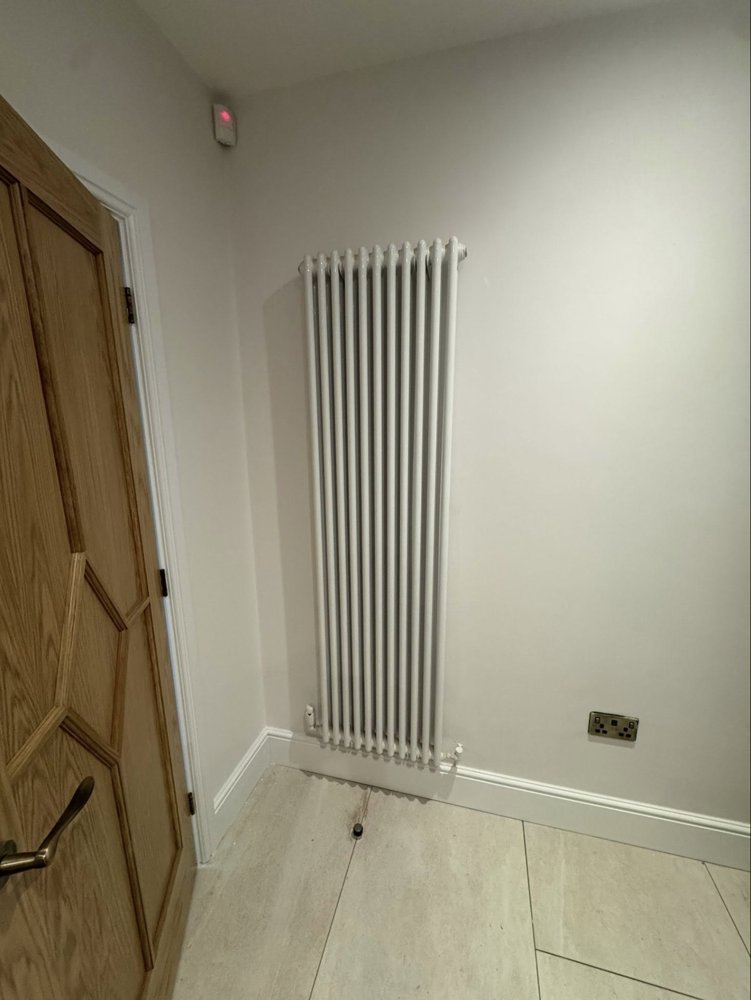 A tall white vertical column radiator in a hallway